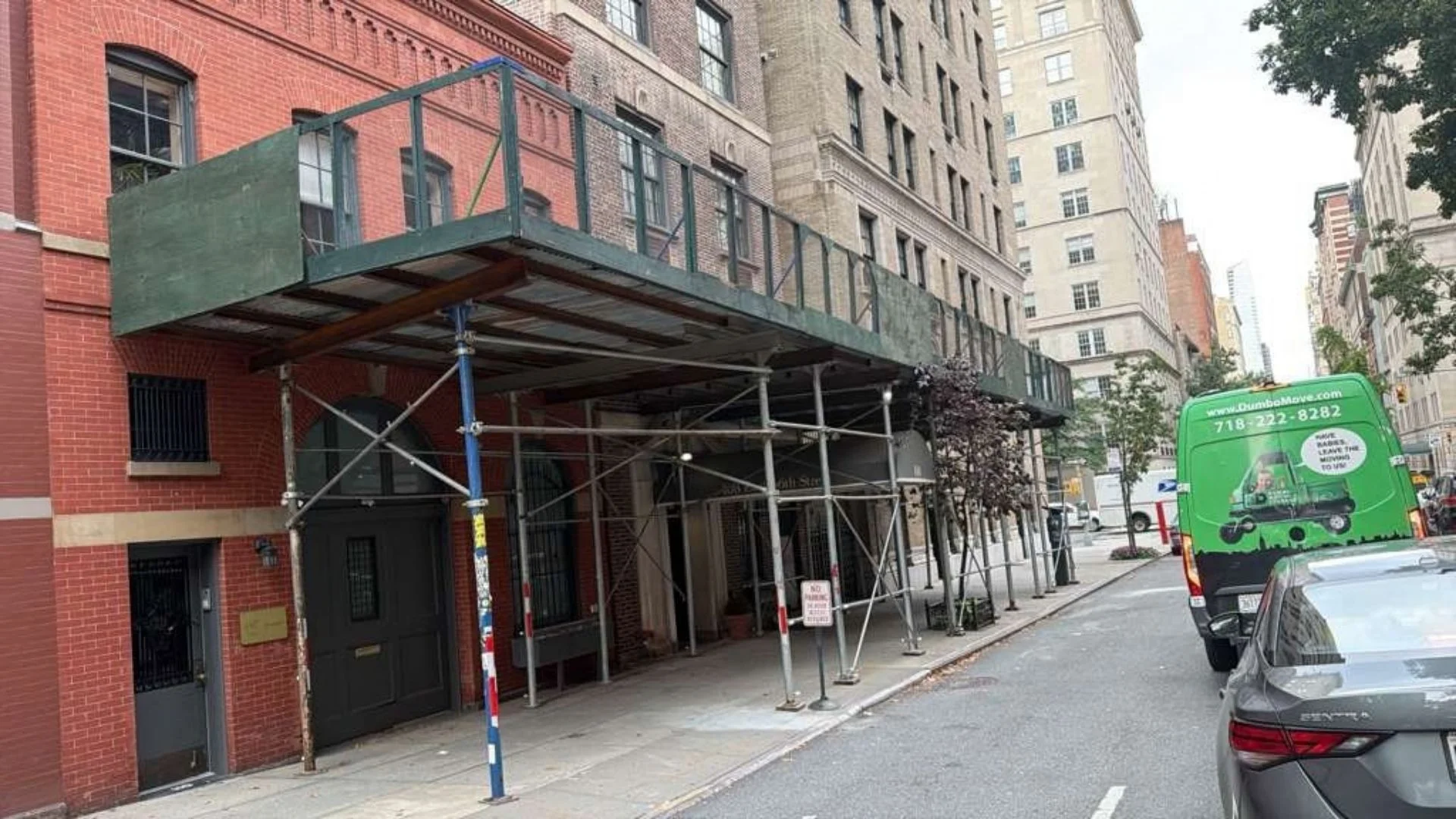 Bronx Sidewalk Shed and Scaffolding sidewalk shed care and maintenance for a green plywood shed with steel deck, guardrail and pipe scaffolding at a city street corner